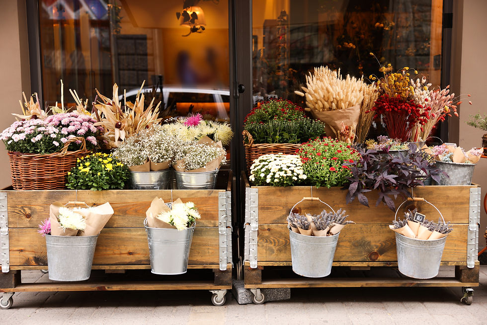 Flower shop window display of colorful bouquets and dried flowers in metal buckets and wicker baskets on wooden carts.