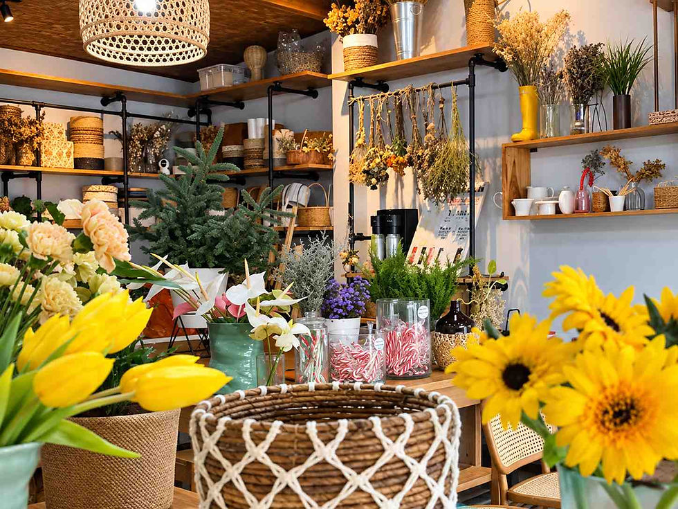 Bright flower shop filled with yellow tulips, sunflowers, dried arrangements, and woven baskets on wooden shelves.